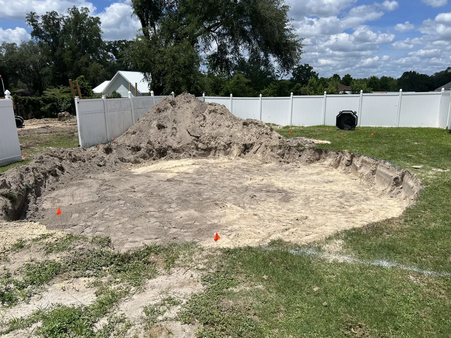 Excavated ground and a soil pile within the same fenced backyard.