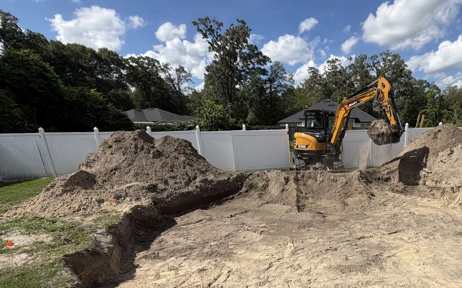 Falcon excavator moving soil within a marked backyard excavation.